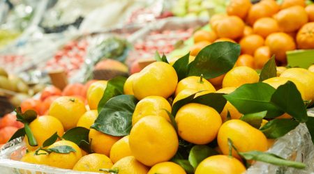 Background image of fruit stand at farmers market, heap of ripe tangerines decorated with laves in focus, copy space