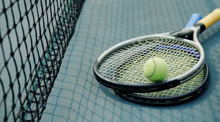 Two tennis rackets and ball next to the net on tennis court